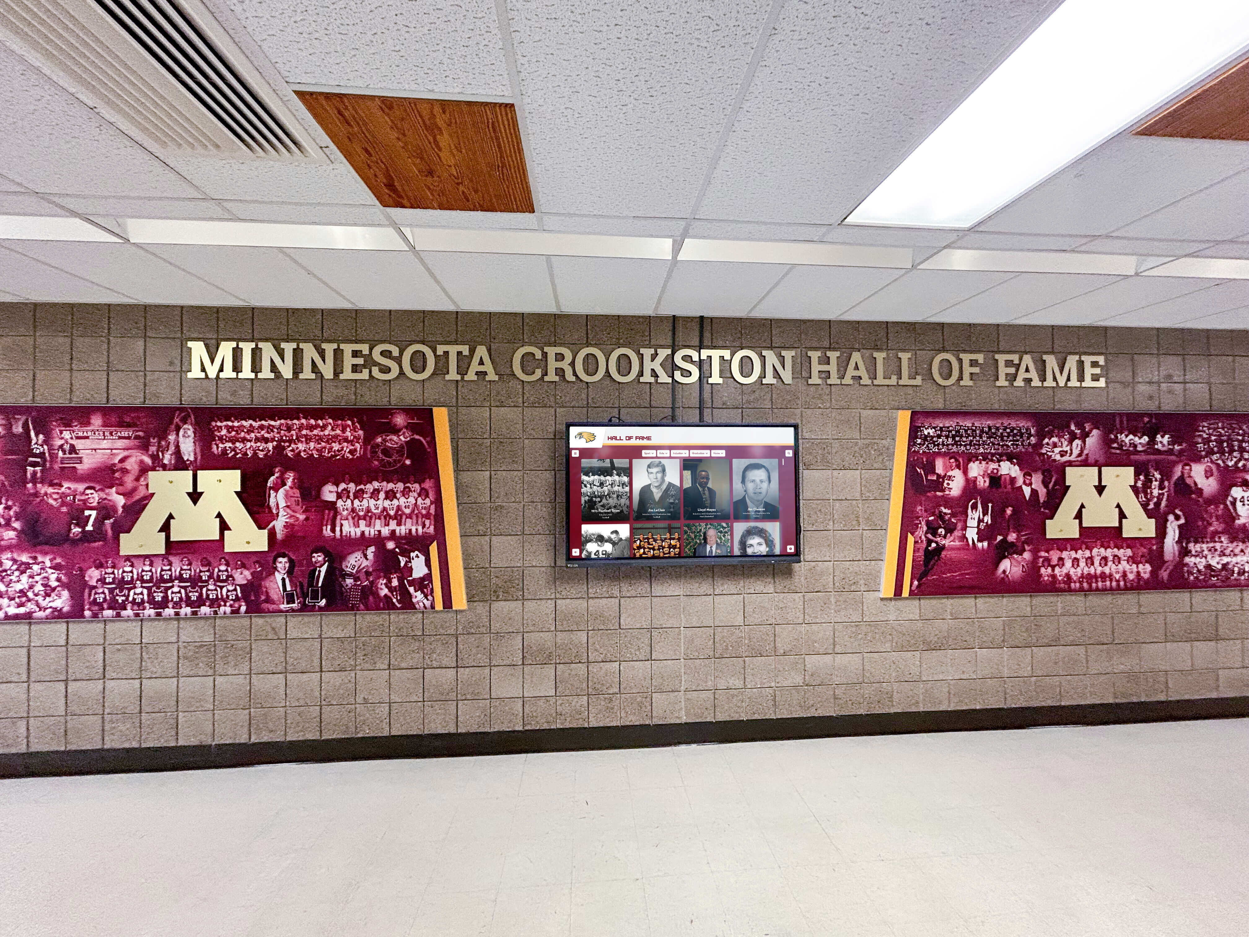 Minnesota Crookston athletics facility featuring branded maroon murals with integrated digital recognition display Minnesota Crookston hall of fame with maroon murals and digital recognition screen
