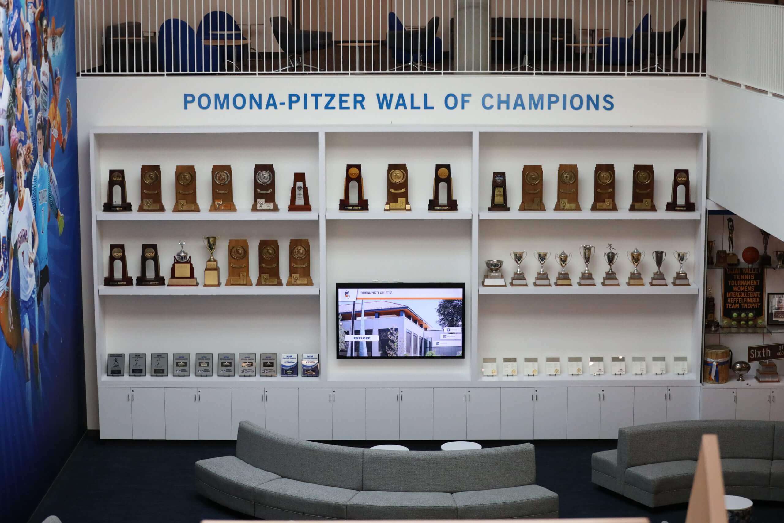 Wall of champions recognition space with championship trophies and recognition displays — the material selection decisions made for each championship banner determine how that element holds up as part of the permanent record over years and decades of display Pomona-Pitzer Wall of Champions trophy display lounge with championship trophies and recognition displays alongside athletic seating areas