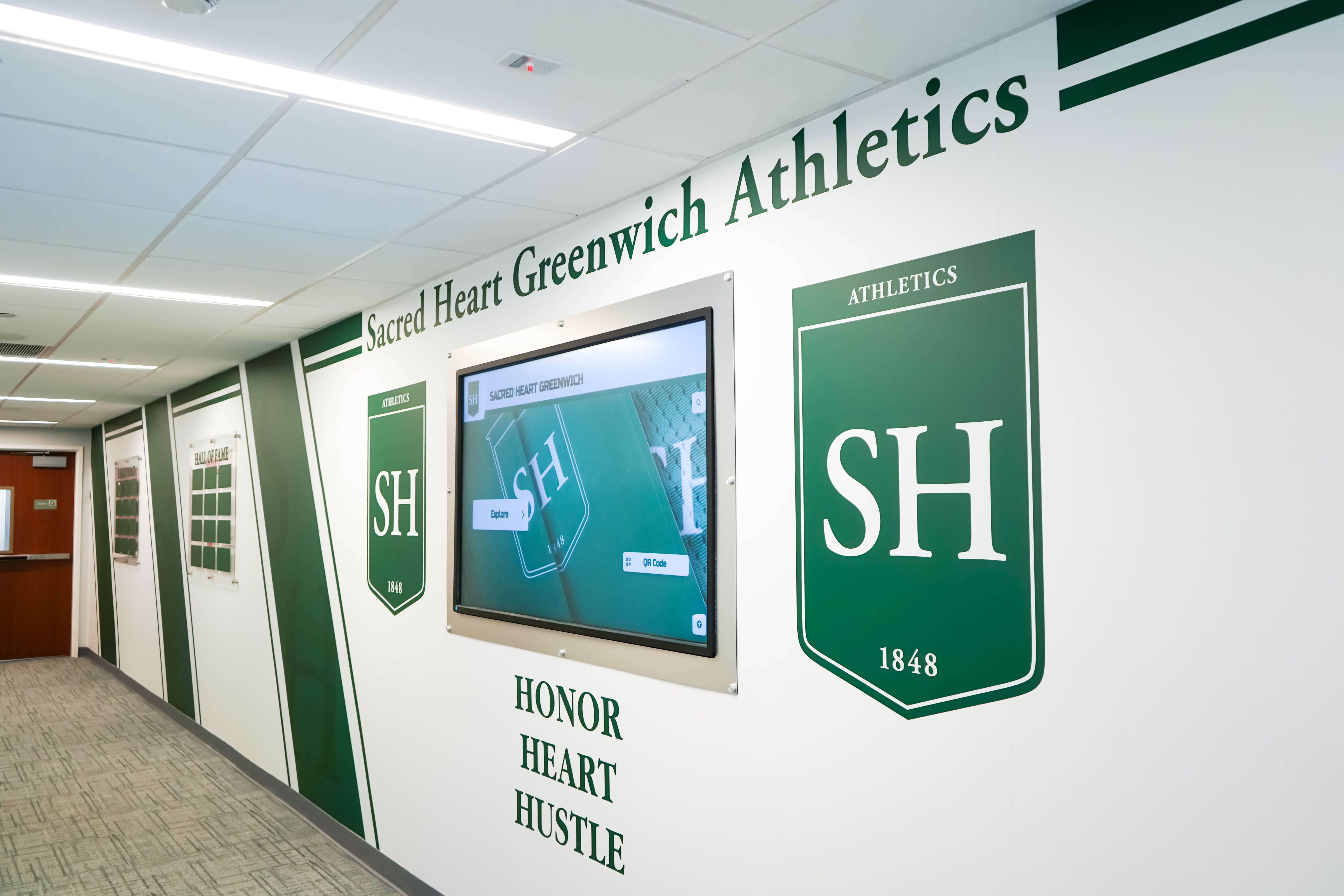 School hallway featuring organized shield recognition displays for academic and achievement programs Sacred Heart Greenwich athletics hallway shield display showing organized recognition panels