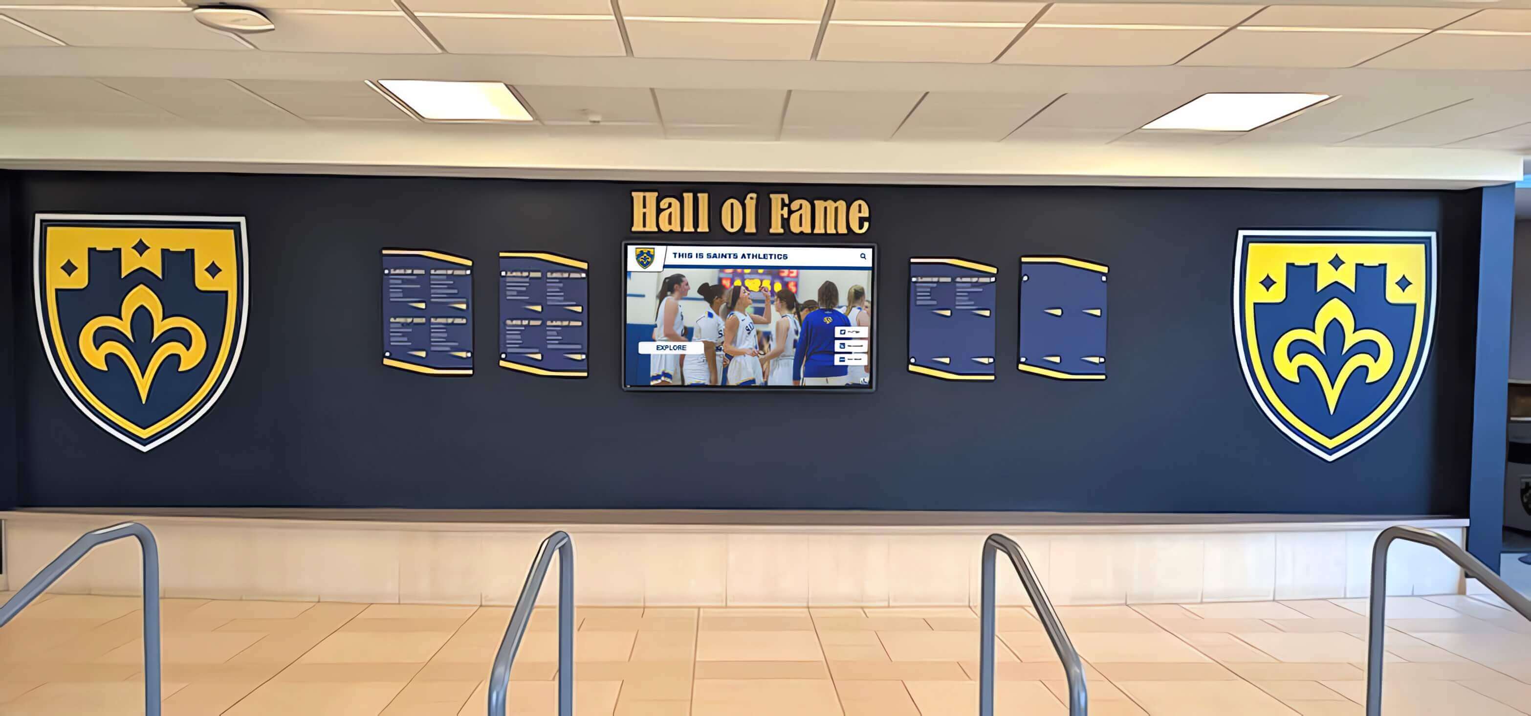 School lobby recognition wall in blue and gold featuring shield displays and integrated digital screen School hall of fame lobby wall with blue and yellow shields and TV display