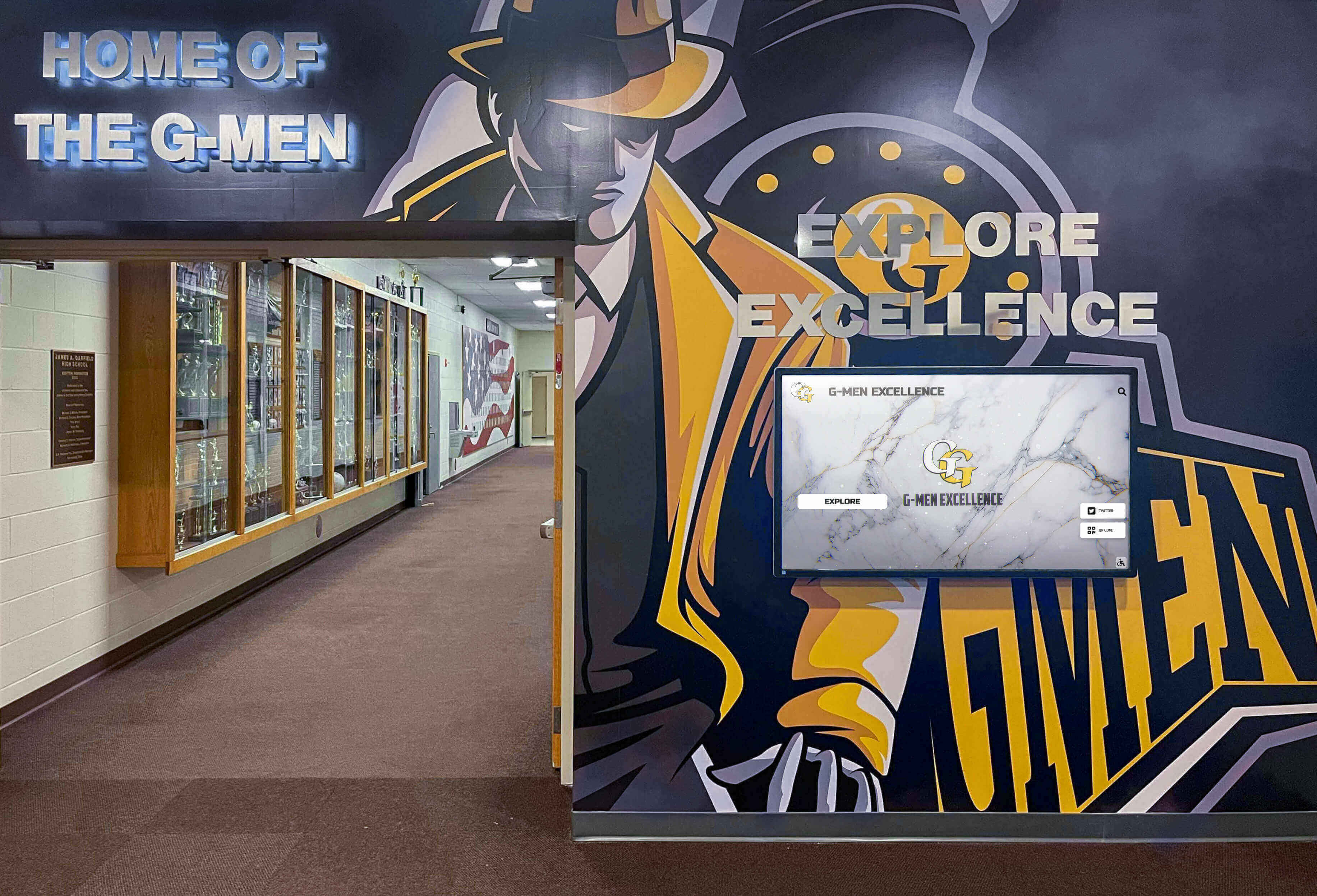 School hallway featuring branded G-Men athletic mural alongside digital displays and traditional trophy cases G-Men school hallway mural with digital display and trophy cases