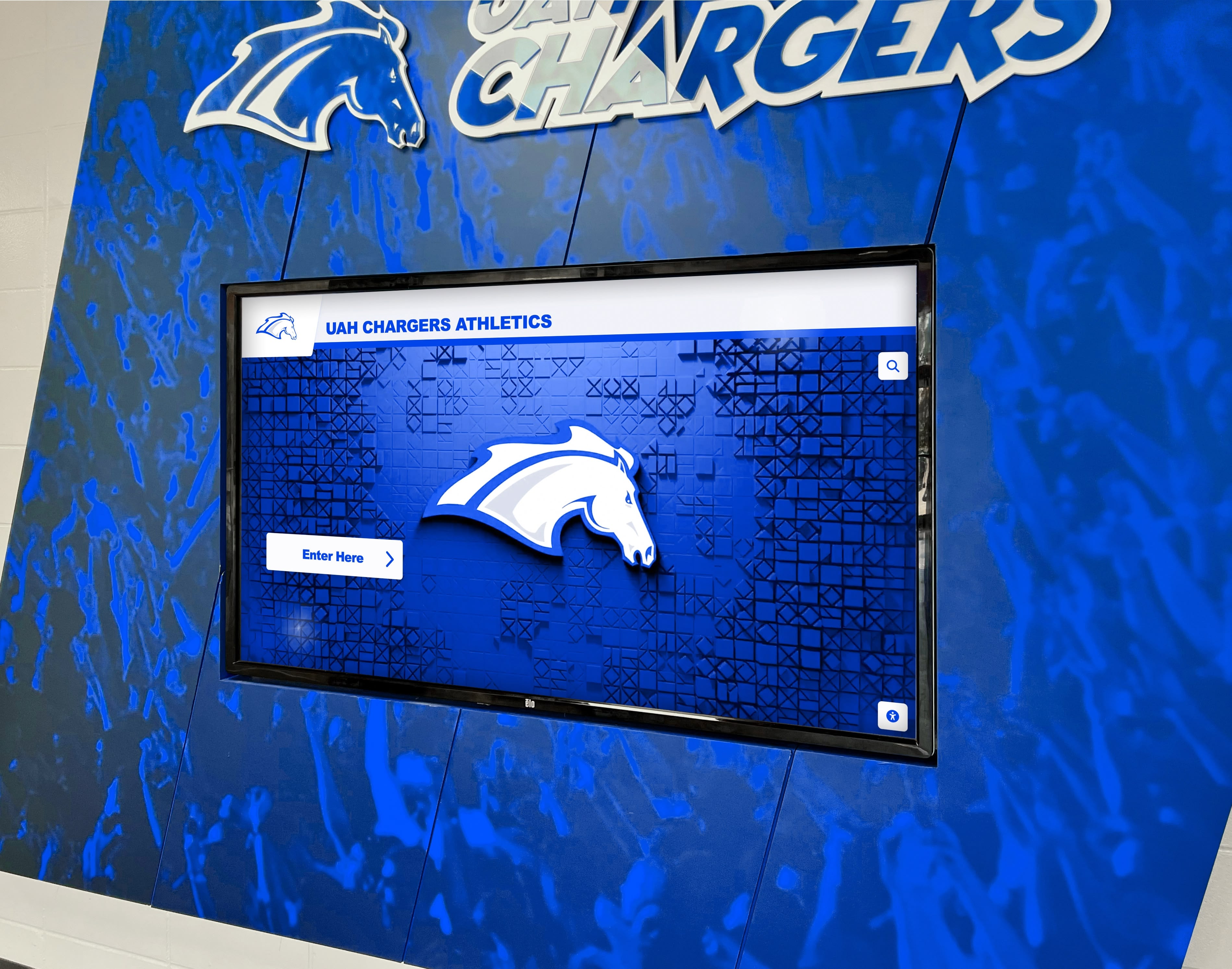 Digital athletics recognition screen integrated into school wall display — a modern format for presenting program achievement and unit history to the full school community UAH Chargers athletics digital screen on blue wall